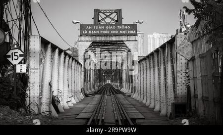 Una vista lungo i binari ferroviari attraverso il ponte arrugginito Long Bien ad Hanoi, Vietnam. Il cartello recita: La sicurezza stradale è la felicità di ogni casa Foto Stock