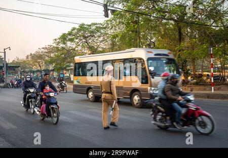 Un poliziotto attraversa Yen Phu Road tra le motociclette e un autobus ad Hanoi, in Vietnam. Foto Stock