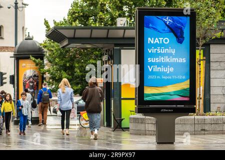 Banner pubblicitario che informa sul prossimo vertice NATO 2023 nel centro di Vilnius, capitale della Lituania, con ragazze e bambini che camminano nelle vicinanze Foto Stock