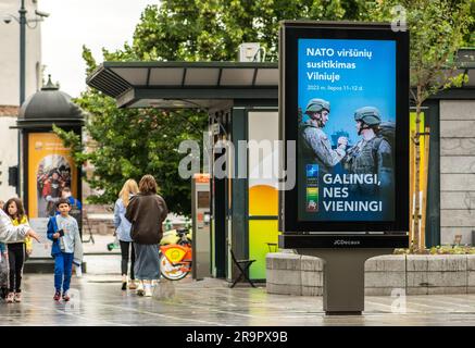 Banner pubblicitario che informa sul prossimo vertice NATO 2023 nel centro di Vilnius, capitale della Lituania, con ragazze e bambini che camminano nelle vicinanze Foto Stock