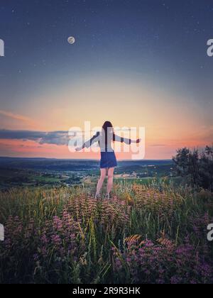 Concetto giovanile selvaggio e libero con una ragazza rilassata, la vista posteriore si staglia con le mani allungate di fronte al bellissimo tramonto estivo sulla cima di una collina Foto Stock