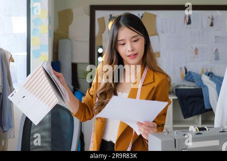 Stilista donna che lavora sui suoi progetti in uno studio di officina, imprenditrice femminile con abiti, imprenditrice sartoriale, negozio di abbigliamento Foto Stock