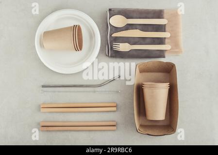 Set di stoviglie ecologiche e imballaggi in carta kraft per alimenti su sfondo di cemento chiaro. Imballaggi di carta per alimenti di strada - tazze, piatti, cannucce, contengono Foto Stock