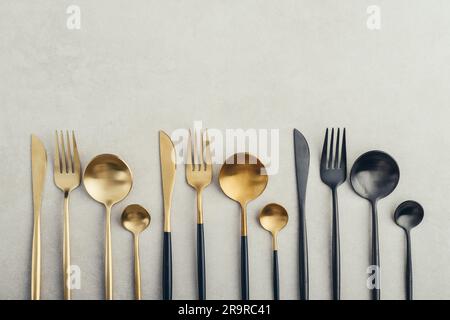 Set di posate di colore dorato e nero con forchetta, coltello, cucchiaio e cucchiaio da tè su sfondo in cemento. Foto Stock