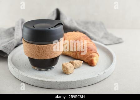 Caffè da asporto in tazza da viaggio riutilizzabile in vetro e fascia in sughero con croissant su vassoio Zero sprechi. Concetto di stile di vita sostenibile. Foto Stock