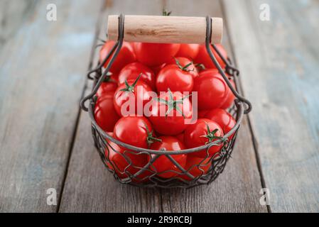 Pomodori ciliegini in un cesto di metallo d'epoca su fondo di legno Foto Stock