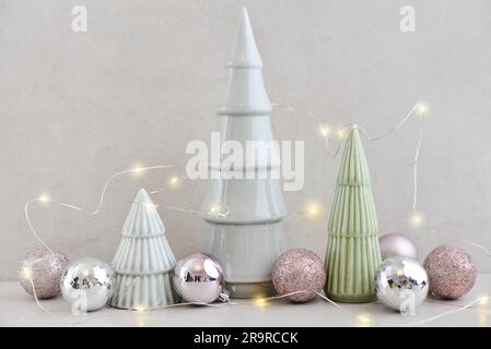 Abeti decorativi in ceramica con palline di natale e ramoscelli di abete su sfondo chiaro Foto Stock
