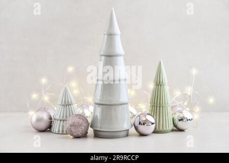 Abeti decorativi in ceramica con palline di natale e ramoscelli di abete su sfondo chiaro Foto Stock