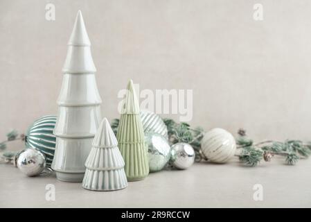 Abeti decorativi in ceramica con palline di natale e ramoscelli di abete su sfondo chiaro Foto Stock