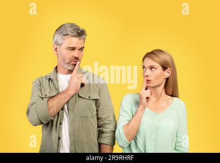 Shh, silenzio. Coppia europea di mezza età che gestiva il segno di hush, guardandosi l'un l'altro e tenendo il dito sulle labbra Foto Stock