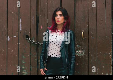 Un'elegante femmina si trova di fronte a un cancello di ferro ornamentale, sorridendo con sicurezza per la fotocamera Foto Stock