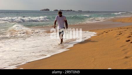 Sri Lanka, Hikkaduwa-12 dicembre 2019: Un surfista cammina lungo la riva del mare di Laccadive con una tavola da surf nella zona di surf Foto Stock