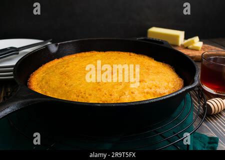 Pane di mais al burro cotto in uno sciroppo di ghisa a un angolo basso: Pane di mais del Sud appena fatto in una padella con burro e miele a lato Foto Stock