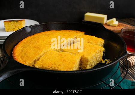 Pane di mais al burro al forno tagliato a pezzi in un pezzetto di ghisa: Pane di mais del Sud appena fatto in una padella con burro e miele a lato Foto Stock