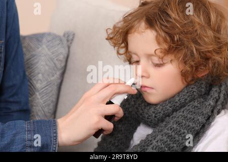 Madre che usa lo spray nasale per trattare il suo bambino sul divano, primo piano Foto Stock