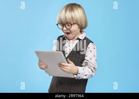 Simpatico bambino in occhiali con un tablet su sfondo azzurro Foto Stock