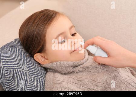 Madre che usa lo spray nasale per trattare la sua bambina sul divano, primo piano Foto Stock