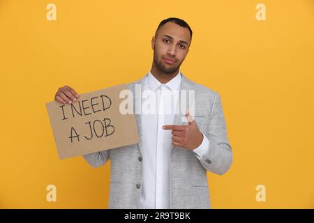 Giovane disoccupato con un cartello con la frase ho bisogno di Un lavoro su sfondo giallo Foto Stock