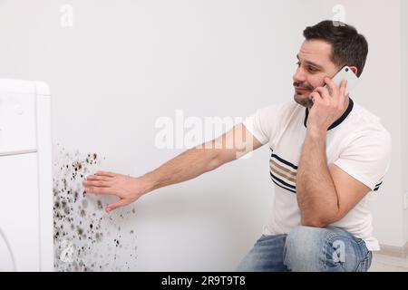 Servizio di rimozione dello stampo. Uomo che parla al telefono e guarda il muro interessato nella stanza Foto Stock