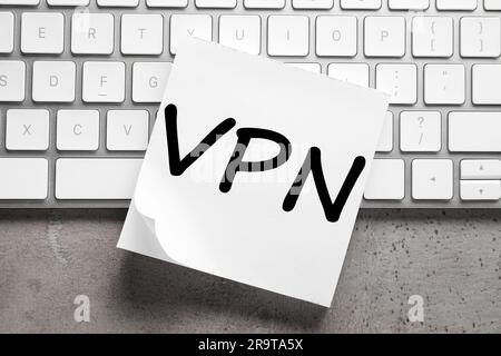 Foglio di carta con acronimo VPN (Virtual Private Network) e tastiera su tavola grigia, vista dall'alto Foto Stock