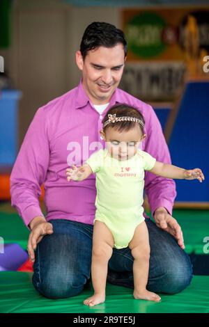 Bella bambina di dieci mesi che impara a camminare aiutata da suo padre. Concetto di stimolazione precoce per i bambini piccoli. Foto Stock