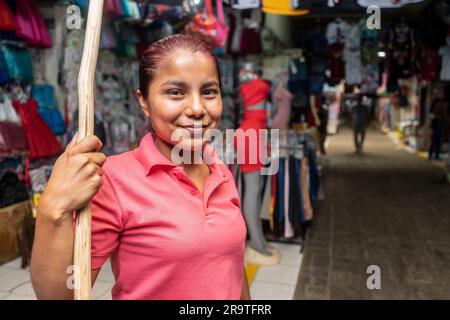 Concessionario di fronte a un tratto di abbigliamento con un bastoncino di legno per posizionare gli indumenti in un mercato tradizionale in Nicaragua Foto Stock