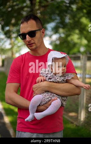 Padre che cammina in un parco e tiene piccola bambina Foto Stock