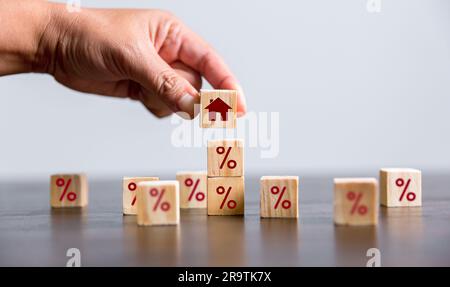 Costruire a mano una casa con cubetti di legno con il segno di percentuale su di loro. Nozione di tassi di interesse sui mutui ipotecari finanziari, mutui per la casa, rifinanziamento delle abitazioni, Foto Stock