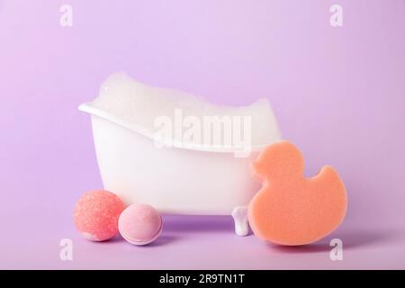 Piccola vasca da bagno con schiuma, spugna e bombe da bagno su sfondo lilla  Foto stock - Alamy