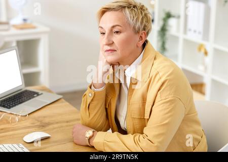 Donna matura e premurosa seduta al tavolo in ufficio Foto Stock
