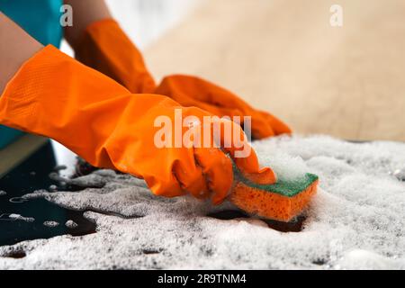 Donna con guanti di gomma arancione che pulisce la stufa elettrica con spugna Foto Stock