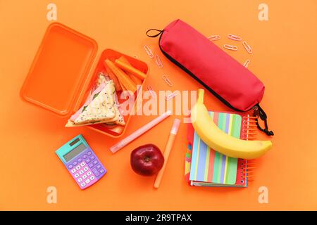 Cancelleria diversa e pranzo al sacco con gustosi piatti su sfondo arancione Foto Stock