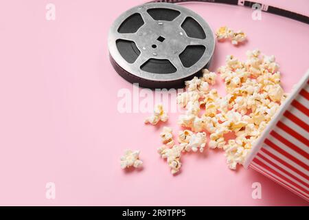 Secchiello con gustosi popcorn e pellicola su sfondo rosa Foto Stock