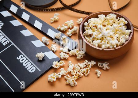 Ciotola con gustosi popcorn, clapperboard e bobina di pellicola su sfondo marrone Foto Stock