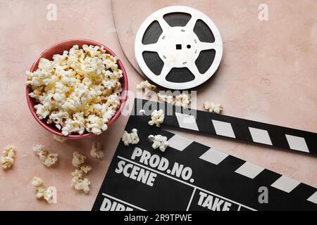 Ciotola con gustosi popcorn, clapperboard e bobina di pellicola su sfondo chiaro Foto Stock