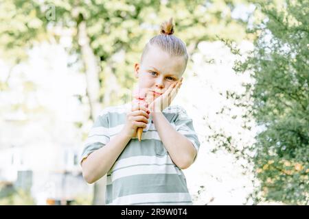 Un bambino triste stringeva la guancia con la mano e teneva un cono gelato nell'altra mano. Problemi di sensibilità dei denti in un bambino o di decadimento dei denti. Foto Stock