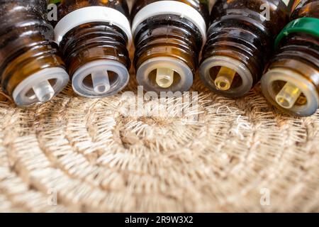 5 flaconi contagocce di olio essenziale versati in una linea su un placemat circolare con corda di iuta, macro di messa a fuoco morbida Foto Stock