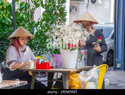 Febbraio 25 2023 - George Town - Penang-Malesia - bellissime giovani donne con cappelli da sole tradizionali organizzano fiori da offrire in vendita Foto Stock