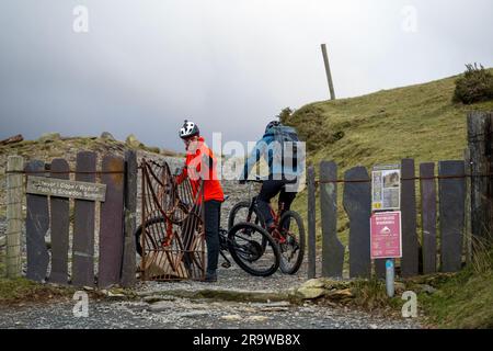 Due uomini cavalcano in mountain bike lungo il sentiero Llanberis fino alla cima del monte Snowdon (Yr Wyddfa) a Snowdonia, Galles, a febbraio. Foto Stock