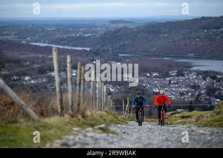 Due uomini cavalcano in mountain bike lungo il sentiero Llanberis fino alla cima del monte Snowdon (Yr Wyddfa) a Snowdonia, Galles, a febbraio. Foto Stock