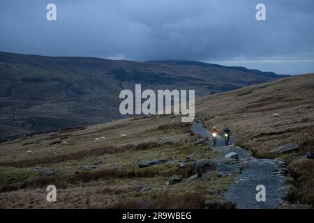 Due uomini cavalcano in mountain bike lungo il sentiero Llanberis fino alla cima del monte Snowdon (Yr Wyddfa) a Snowdonia, Galles, a febbraio. Foto Stock