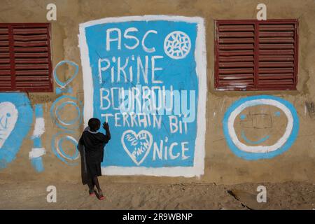 Un ragazzo di fronte a un muro dipinto in un villaggio di pescatori a Dakar, in Senegal Foto Stock