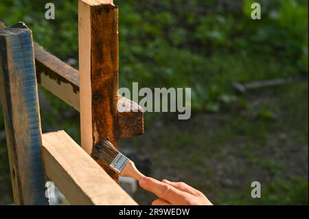 Uomo dipinge con pittura le travi di legno per recinzione di legno Foto Stock