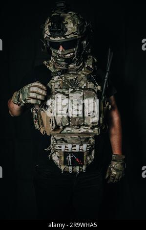 Un soldato determinato, in uniforme mimetica completa e con un casco tattico, è pronto con una pistola, pronto ad affrontare qualsiasi sfida Foto Stock