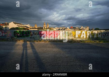 Lunghe ombre su una recinzione ricoperta di graffiti al tramonto in una giornata nuvolosa a Lugo, in Galizia Foto Stock