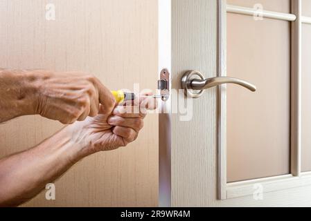 Un uomo sta montando il colpo di protezione del catenaccio su una porta in vetro con una moderna maniglia curva in nichel utilizzando un cacciavite Foto Stock