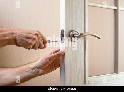 Un uomo sta montando il colpo di protezione del catenaccio su una porta in vetro con una moderna maniglia curva in nichel utilizzando un cacciavite Foto Stock