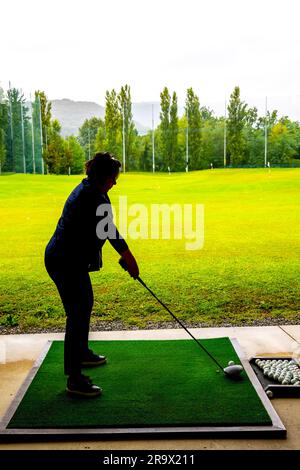 Golfista che allena il suo pilota di golf club sul campo pratica in una giornata di pioggia in Svizzera Foto Stock