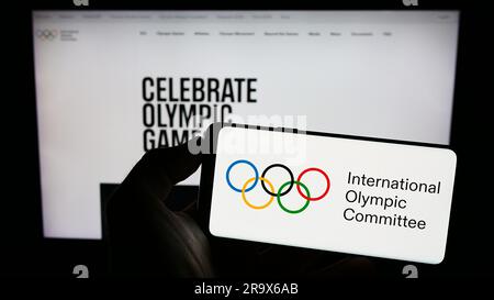 Persona in possesso di un cellulare con il logo del Comitato Olimpico Internazionale (CIO) sullo schermo davanti alla pagina web. Concentrarsi sul display del telefono. Foto Stock