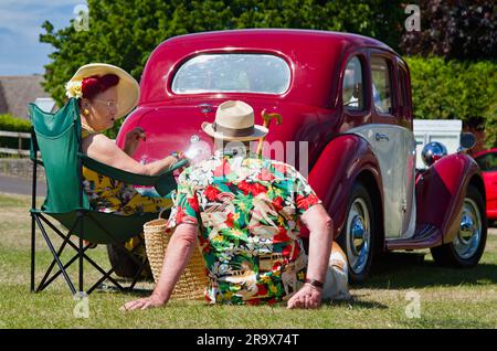 Uomo e donna in abiti vintage anni '1940, anni '1950 seduti sull'erba accanto a Una Classic Vintage Car, Christchurch Inghilterra Regno Unito Foto Stock